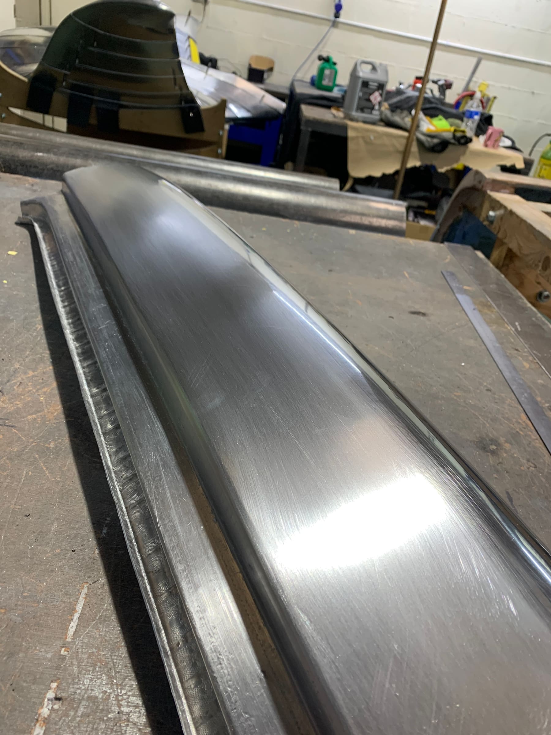 A finished hand-formed aluminium panel resting on the workshop bench
