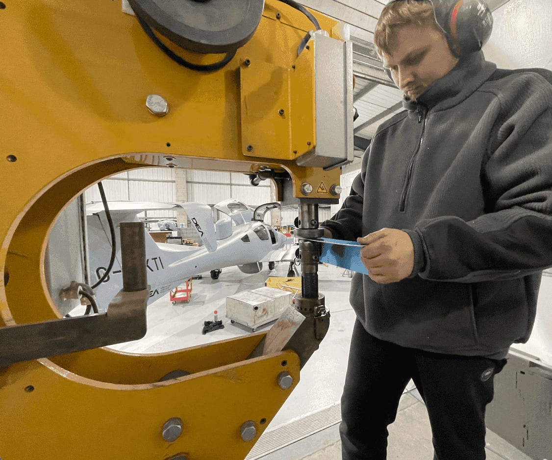 Toby Southan forming a metal panel on a press, with an aircraft under build in the background
