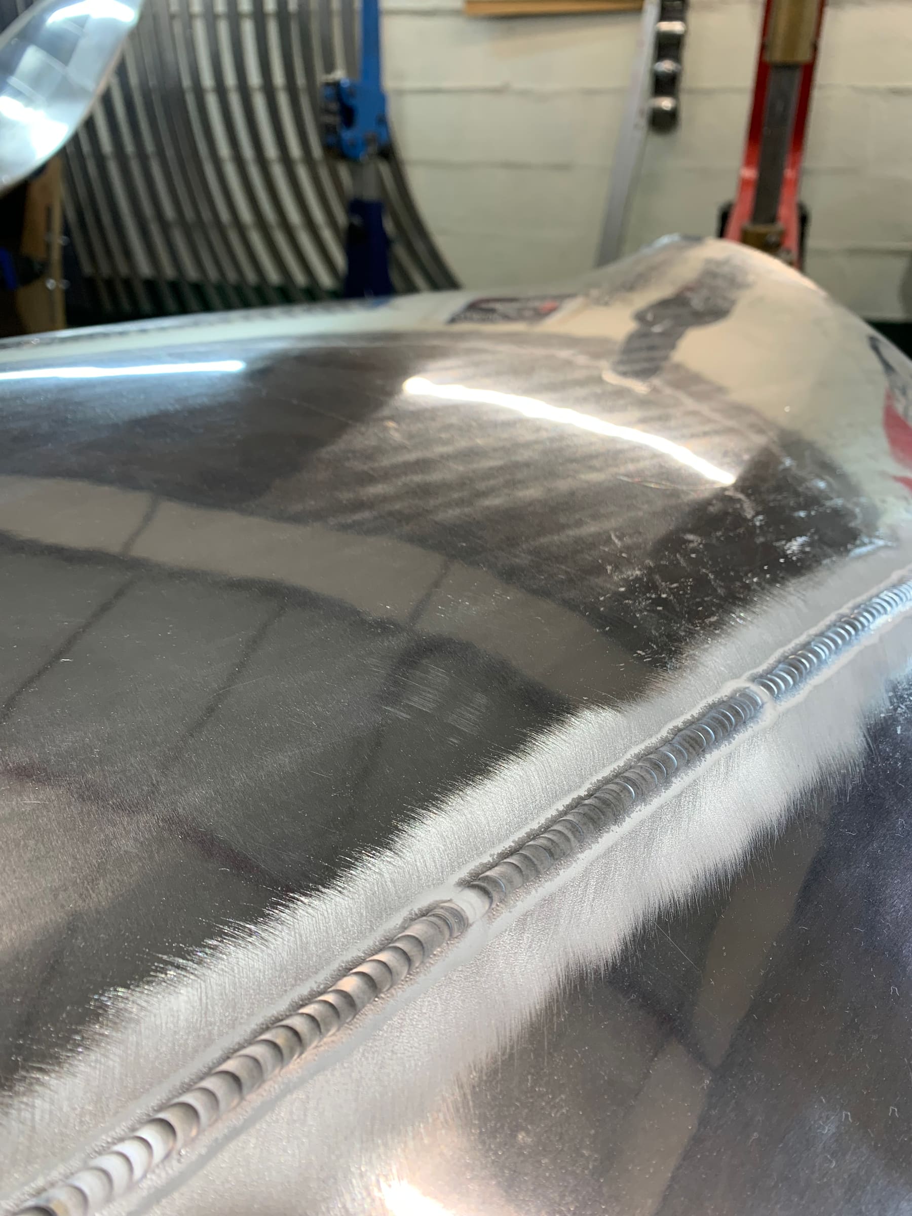 Close-up detail of a hand-finished welded seam on a curved aluminium body panel
